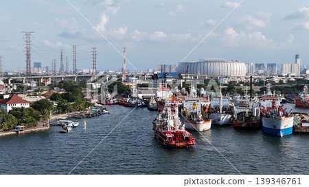 a red offshore supply and rescue ship equipped with a lattice tower, docked at a busy industrial port alongside various barges and heavy maritime equipment. a red offshore supply and rescue ship equipped with a lattice tower, docked at a busy industrial port alongside various barges and heavy maritime equipment. 139346761
