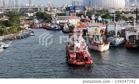 a red offshore supply and rescue ship equipped with a lattice tower, docked at a busy industrial port alongside various barges and heavy maritime equipment. a red offshore supply and rescue ship equipped with a lattice tower, docked at a busy industrial port alongside various barges and heavy maritime equipment. 139347742