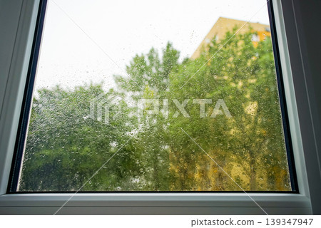 Raindrops on a window pane showing greenery n the background on a cloudy day Raindrops on a window pane showing greenery n the background on a cloudy day 139347947