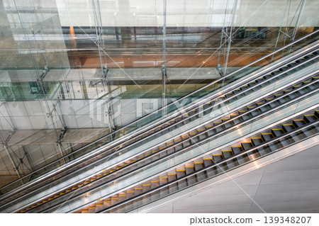 Escalators inside glass architectural space with reflections and lines Escalators inside glass architectural space with reflections and lines 139348207