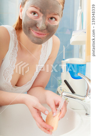 woman removing facial clay mud mask in bathroom woman removing facial clay mud mask in bathroom 139348339