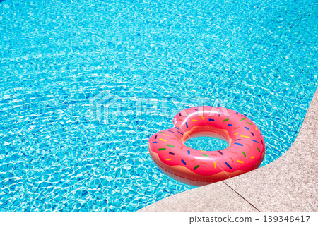 Pink donut inflatable ring floating in blue swimming pool water summer concept Pink donut inflatable ring floating in blue swimming pool water summer concept 139348417