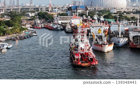 a red offshore supply and rescue ship equipped with a lattice tower, docked at a busy industrial port alongside various barges and heavy maritime equipment. a red offshore supply and rescue ship equipped with a lattice tower, docked at a busy industrial port alongside various barges and heavy maritime equipment. 139348441