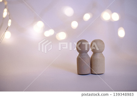 Two wooden figurines standing close together against a blurred background of warm fairy lights, creating a cozy and inviting atmosphere Two wooden figurines standing close together against a blurred background of warm fairy lights, creating a cozy and inviting atmosphere 139348983