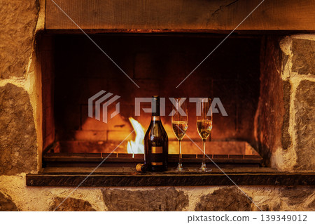 Elegant champagne bottle with two flutes placed on a rustic stone fireplace, warm flames flickering in the background, creating a cozy and inviting atmosphere for celebration Elegant champagne bottle with two flutes placed on a rustic stone fireplace, warm flames flickering in the background, creating a cozy and inviting atmosphere for celebration 139349012