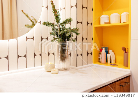 Modern bathroom interior featuring a stylish countertop with a vase of greenery, candles, and beauty products, complemented by geometric patterned tiles and vibrant yellow accents Modern bathroom interior featuring a stylish countertop with a vase of greenery, candles, and beauty products, complemented by geometric patterned tiles and vibrant yellow accents 139349017