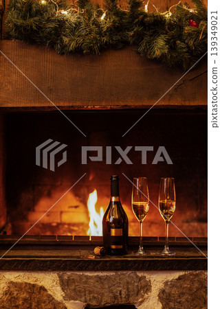 Close-up of two glasses of champagne on the fireplace. A bottle of sparkling wine and goblets near an open fire. The Christmas party or a romantic meeting. Close-up of two glasses of champagne on the fireplace. A bottle of sparkling wine and goblets near an open fire. The Christmas party or a romantic meeting. 139349021