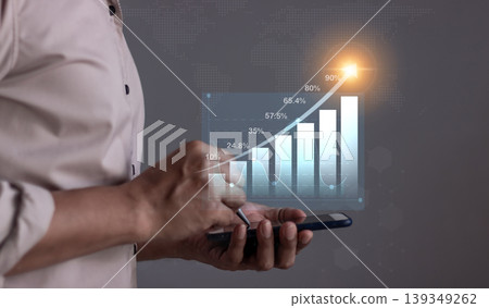 Young man with smartphone hand touching to visualize money growth The phone screen displays graphs and charts showing increasing investment and savings trends, along with an increased account balance Young man with smartphone hand touching to visualize money growth The phone screen displays graphs and charts showing increasing investment and savings trends, along with an increased account balance 139349262