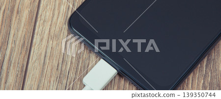 Black smartphone and connected cable of charger. Telephone charging Black smartphone and connected cable of charger. Telephone charging 139350744