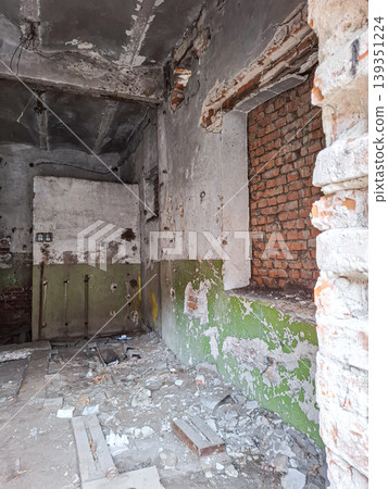The room shows crumbling plaster walls and exposed red bricks. Debris is scattered on the floor. The space has not been used for a long time. There are signs of decay and neglect. The room shows crumbling plaster walls and exposed red bricks. Debris is scattered on the floor. The space has not been used for a long time. There are signs of decay and neglect. 139351224