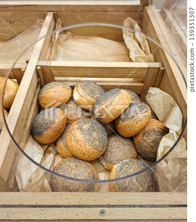 Fresh round bread rolls topped with blue poppy seeds sit in a wooden display bin. They are warm and ready for customers at a bakery during the day. Fresh round bread rolls topped with blue poppy seeds sit in a wooden display bin. They are warm and ready for customers at a bakery during the day. 139351307