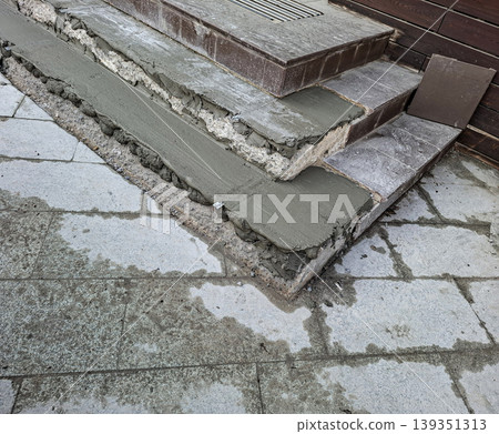 Workers are repairing outdoor stone steps by applying fresh wet cement mortar. The renovation shows a close-up of the steps during the construction process. Workers are repairing outdoor stone steps by applying fresh wet cement mortar. The renovation shows a close-up of the steps during the construction process. 139351313