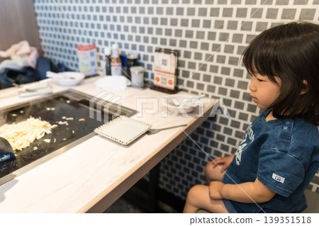 A young Japanese girl eating monjayaki at a teppanyaki restaurant. A young Japanese girl eating monjayaki at a teppanyaki restaurant. 139351518