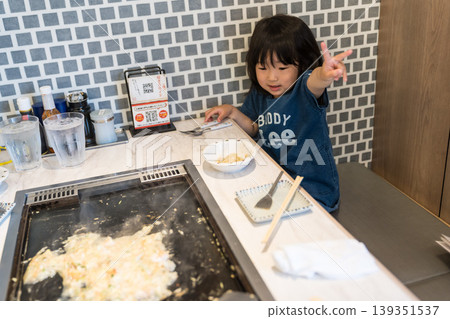 A young Japanese girl eating monjayaki at a teppanyaki restaurant. A young Japanese girl eating monjayaki at a teppanyaki restaurant. 139351537