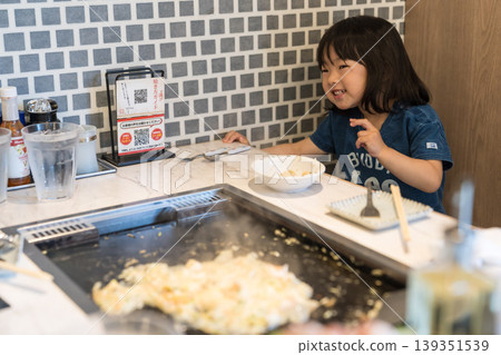 A young Japanese girl eating monjayaki at a teppanyaki restaurant. 139351539