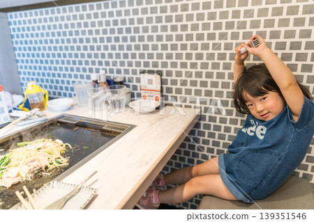 A young Japanese girl eating monjayaki at a teppanyaki restaurant. A young Japanese girl eating monjayaki at a teppanyaki restaurant. 139351546