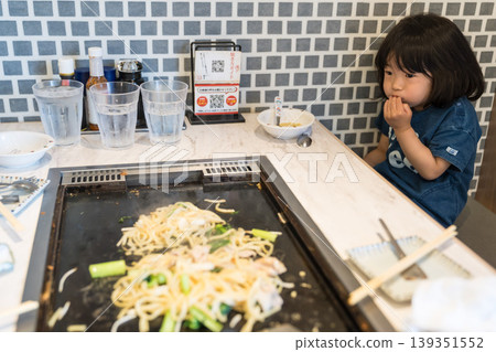 A young Japanese girl eating monjayaki at a teppanyaki restaurant. A young Japanese girl eating monjayaki at a teppanyaki restaurant. 139351552