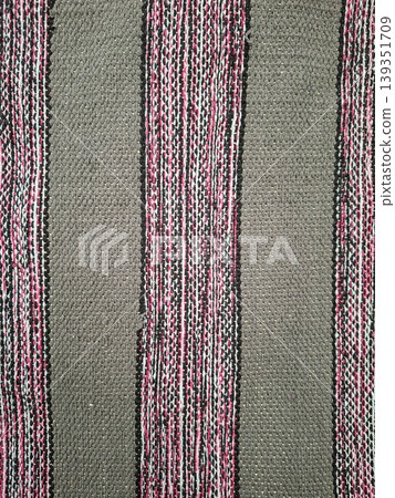 Traditional hand woven grey fabric featuring vertical stripes of black, white, and pink threads. It is often used in clothing and home decor items. 139351709