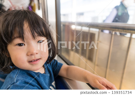 A young Japanese girl looking out the window of a streetcar. 139351734