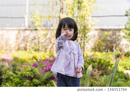 A young Japanese girl smiles in front of a flowerbed. A young Japanese girl smiles in front of a flowerbed. 139351784