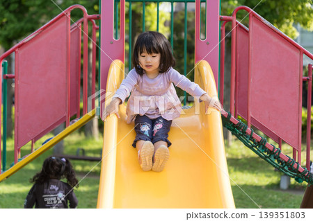 A Japanese toddler girl slides down a slide in a park. A Japanese toddler girl slides down a slide in a park. 139351803