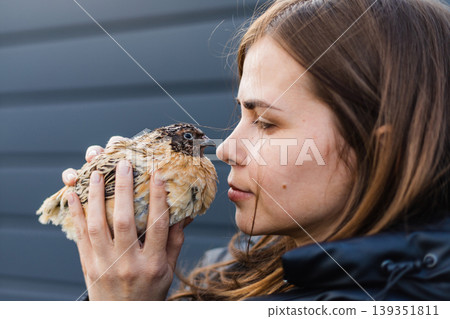 Young woman holds a quail in her hands, touching her nose to its beak. The connection between man and nature. 139351811