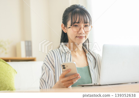A young woman using a computer and a smartphone 139352638