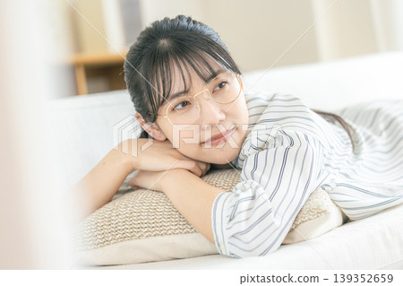 一位戴眼鏡的年輕女子躺在客廳放鬆。 139352659