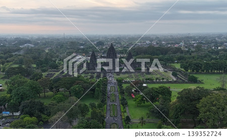 An enchanting evening aerial shot of the Prambanan Hindu Temple complex in Indonesia, featuring its iconic towering stone spires illuminated against a misty twilight sky and a sprawling cityscape. An enchanting evening aerial shot of the Prambanan Hindu Temple complex in Indonesia, featuring its iconic towering stone spires illuminated against a misty twilight sky and a sprawling cityscape. 139352724