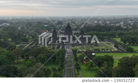 An enchanting evening aerial shot of the Prambanan Hindu Temple complex in Indonesia, featuring its iconic towering stone spires illuminated against a misty twilight sky and a sprawling cityscape. An enchanting evening aerial shot of the Prambanan Hindu Temple complex in Indonesia, featuring its iconic towering stone spires illuminated against a misty twilight sky and a sprawling cityscape. 139352727