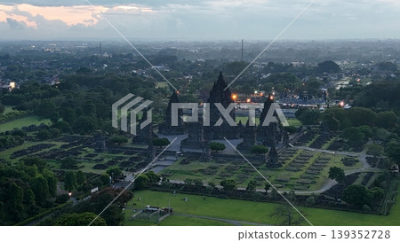An enchanting evening aerial shot of the Prambanan Hindu Temple complex in Indonesia, featuring its iconic towering stone spires illuminated against a misty twilight sky and a sprawling cityscape. An enchanting evening aerial shot of the Prambanan Hindu Temple complex in Indonesia, featuring its iconic towering stone spires illuminated against a misty twilight sky and a sprawling cityscape. 139352728