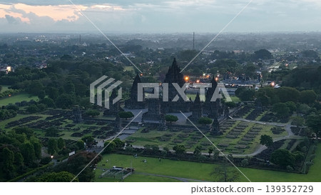 An enchanting evening aerial shot of the Prambanan Hindu Temple complex in Indonesia, featuring its iconic towering stone spires illuminated against a misty twilight sky and a sprawling cityscape. An enchanting evening aerial shot of the Prambanan Hindu Temple complex in Indonesia, featuring its iconic towering stone spires illuminated against a misty twilight sky and a sprawling cityscape. 139352729