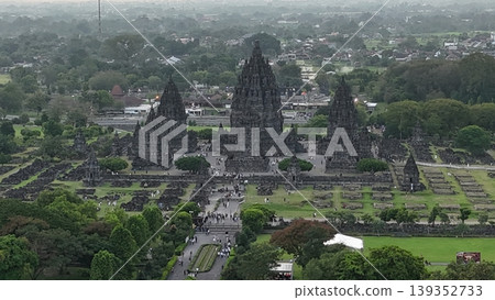 An enchanting evening aerial shot of the Prambanan Hindu Temple complex in Indonesia, featuring its iconic towering stone spires illuminated against a misty twilight sky and a sprawling cityscape. An enchanting evening aerial shot of the Prambanan Hindu Temple complex in Indonesia, featuring its iconic towering stone spires illuminated against a misty twilight sky and a sprawling cityscape. 139352733