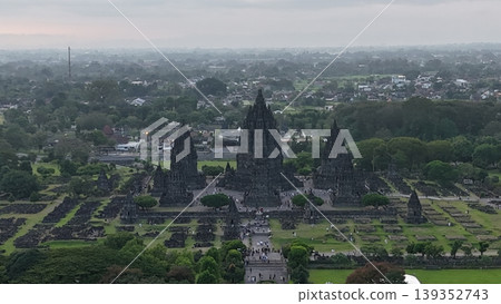 An enchanting evening aerial shot of the Prambanan Hindu Temple complex in Indonesia, featuring its iconic towering stone spires illuminated against a misty twilight sky and a sprawling cityscape. An enchanting evening aerial shot of the Prambanan Hindu Temple complex in Indonesia, featuring its iconic towering stone spires illuminated against a misty twilight sky and a sprawling cityscape. 139352743