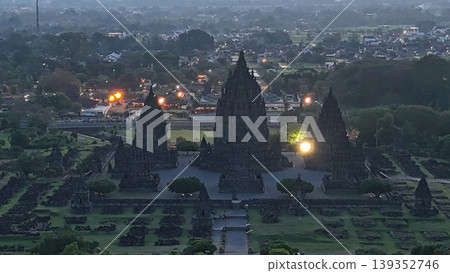 An enchanting evening aerial shot of the Prambanan Hindu Temple complex in Indonesia, featuring its iconic towering stone spires illuminated against a misty twilight sky and a sprawling cityscape. An enchanting evening aerial shot of the Prambanan Hindu Temple complex in Indonesia, featuring its iconic towering stone spires illuminated against a misty twilight sky and a sprawling cityscape. 139352746
