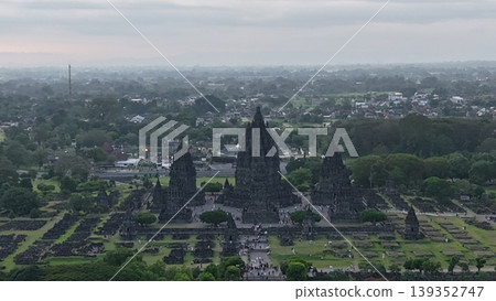 An enchanting evening aerial shot of the Prambanan Hindu Temple complex in Indonesia, featuring its iconic towering stone spires illuminated against a misty twilight sky and a sprawling cityscape. An enchanting evening aerial shot of the Prambanan Hindu Temple complex in Indonesia, featuring its iconic towering stone spires illuminated against a misty twilight sky and a sprawling cityscape. 139352747