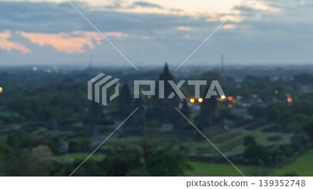 An enchanting evening aerial shot of the Prambanan Hindu Temple complex in Indonesia, featuring its iconic towering stone spires illuminated against a misty twilight sky and a sprawling cityscape. An enchanting evening aerial shot of the Prambanan Hindu Temple complex in Indonesia, featuring its iconic towering stone spires illuminated against a misty twilight sky and a sprawling cityscape. 139352748