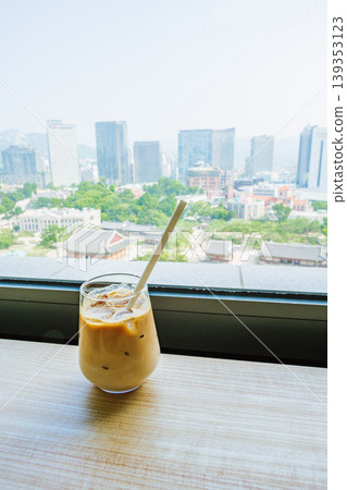 Seoul, South Korea - Jun. 25, 2023 : A refreshing glass of cafe latte at Jeongdong Observatory overlooking the historic palace and city skyline 139353123