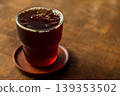 A clear glass of black Americano iced coffee is placed on a wooden table. 139353502
