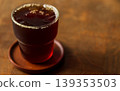 A clear glass of black Americano iced coffee is placed on a wooden table. 139353503