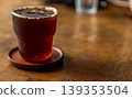 A clear glass of black Americano iced coffee is placed on a wooden table. 139353504