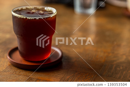 A clear glass of black Americano iced coffee is placed on a wooden table. A clear glass of black Americano iced coffee is placed on a wooden table. 139353504