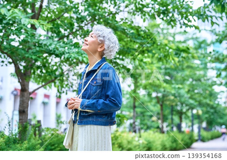 一位老婦人站在綠樹成蔭的街道上，抬頭望向天空。 139354168
