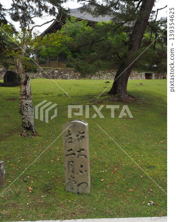 A stone marker guiding visitors through history. It blends seamlessly into the lush greenery of Nara Park, reading "Right: Daifutsu, Left: Nigatsudo." A stone marker guiding visitors through history. It blends seamlessly into the lush greenery of Nara Park, reading "Right: Daifutsu, Left: Nigatsudo." 139354625