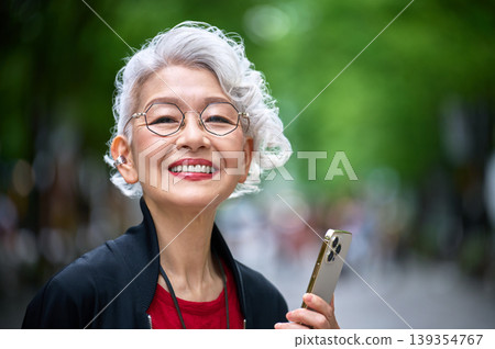 A close-up of a senior woman holding her smartphone and laughing heartily. A close-up of a senior woman holding her smartphone and laughing heartily. 139354767