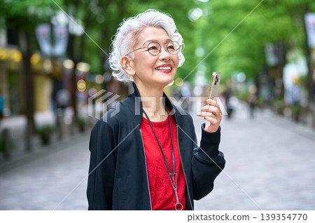 A senior woman looks up, holding her smartphone. 139354770