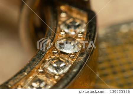 Close view of gold jewelry with clear crystal stones showing fine texture and sparkle under warm light elegant accessory detail with shallow depth of field 139355556