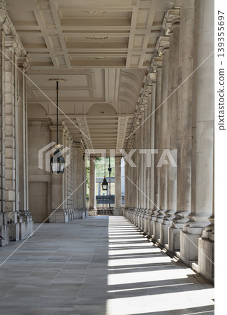 A rhythmic dance of light and shadow unfolds along this majestic colonnade at the Old Royal Naval College, where sunbeams pierce through towering pillars to cast a striking, geometric tapestry upon A rhythmic dance of light and shadow unfolds along this majestic colonnade at the Old Royal Naval College, where sunbeams pierce through towering pillars to cast a striking, geometric tapestry upon 139355697