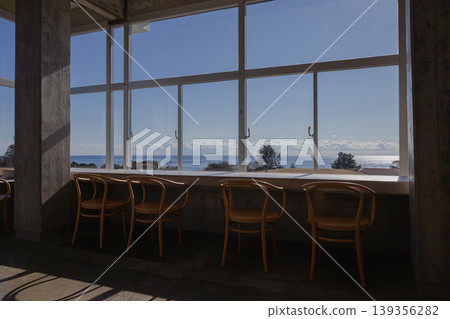 A cafe space where light and shadow play beautifully, with a view of the sea stretching out through large windows. 139356282