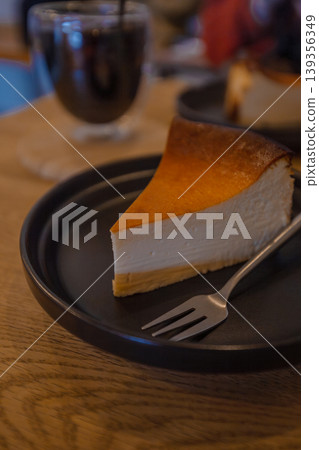 咖啡館裡很受歡迎的甜點:一份濃鬱的巴斯克起司蛋糕配冰咖啡。 咖啡館裡很受歡迎的甜點:一份濃鬱的巴斯克起司蛋糕配冰咖啡。 139356349